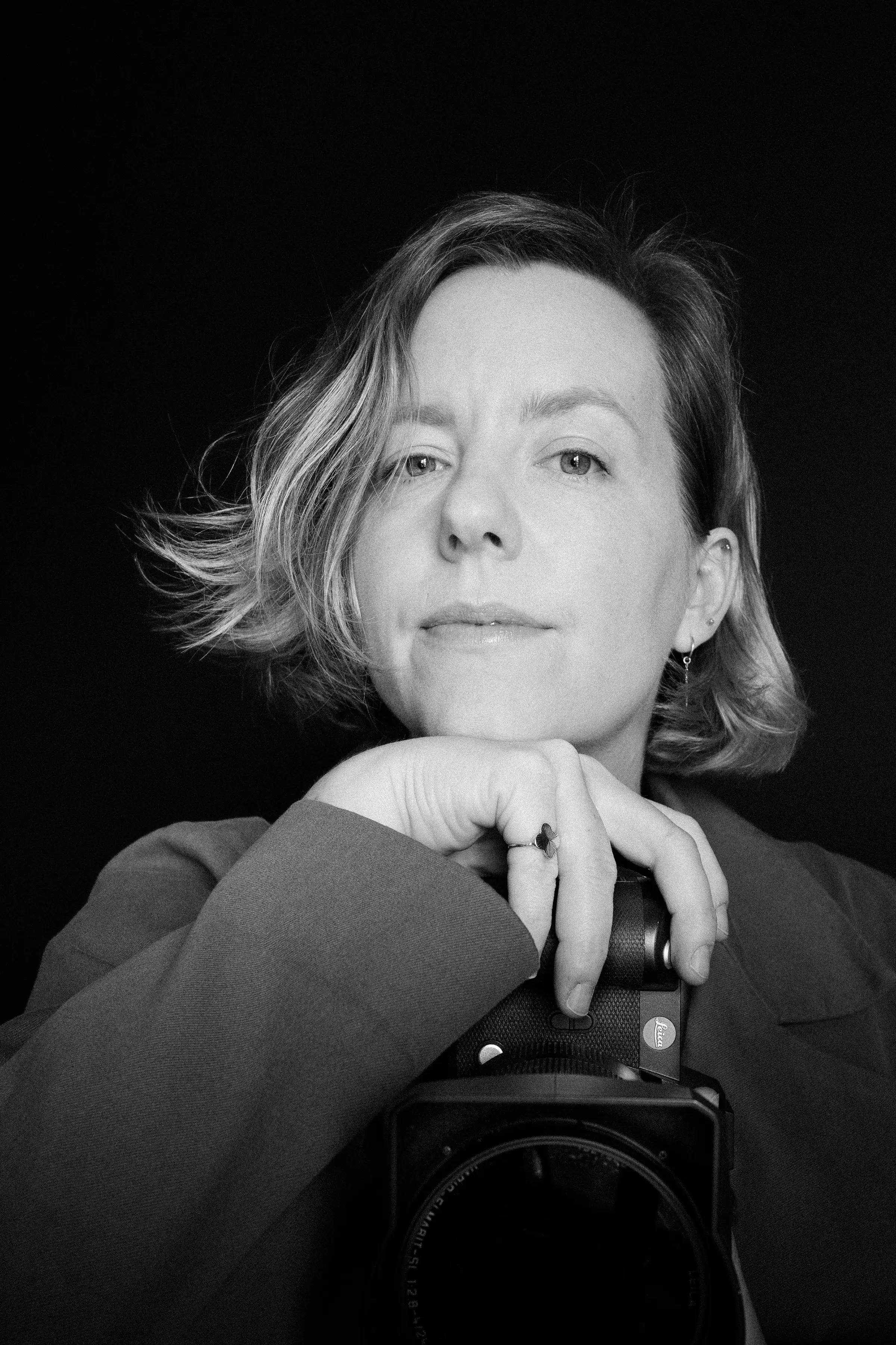 Black and white portrait image of Ivett Dodd with her head resting on her hand and holding her camera.